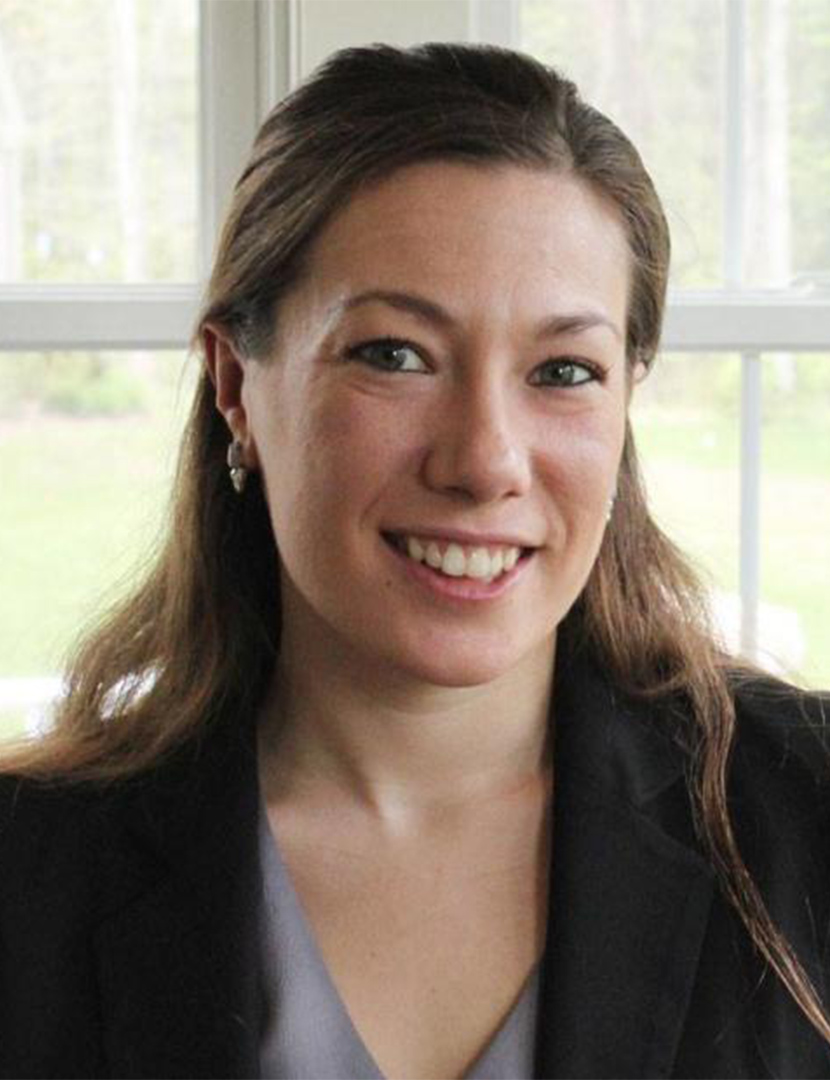 A smiling headshot of a white woman with brown hair wearing a suit jacket.