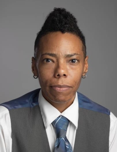 Direct, head-on photo of Commissioner Tanisha Arena, a Black Woman wearing a tie, vest, and collared shirt.
