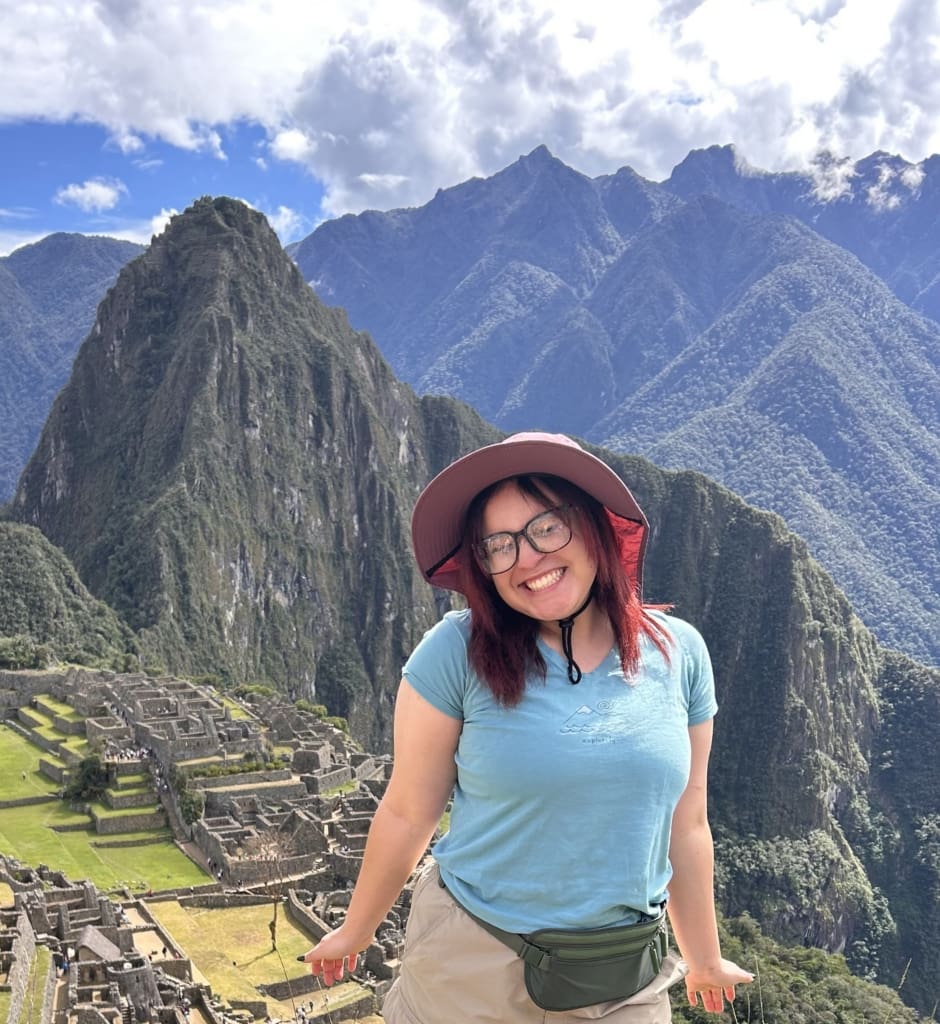A smiling photo of a young latina woman wearing a blue t-shirt in front of a mountain landscape.